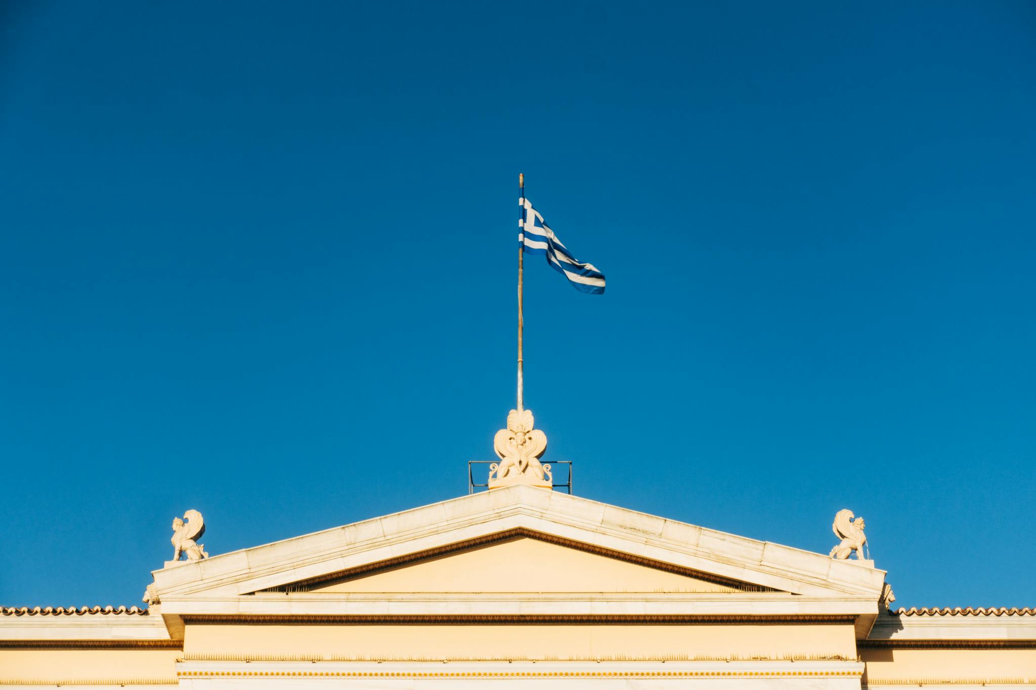 Neoclassical architecture with Greek flag under clear blue sky in Athens, Greece.