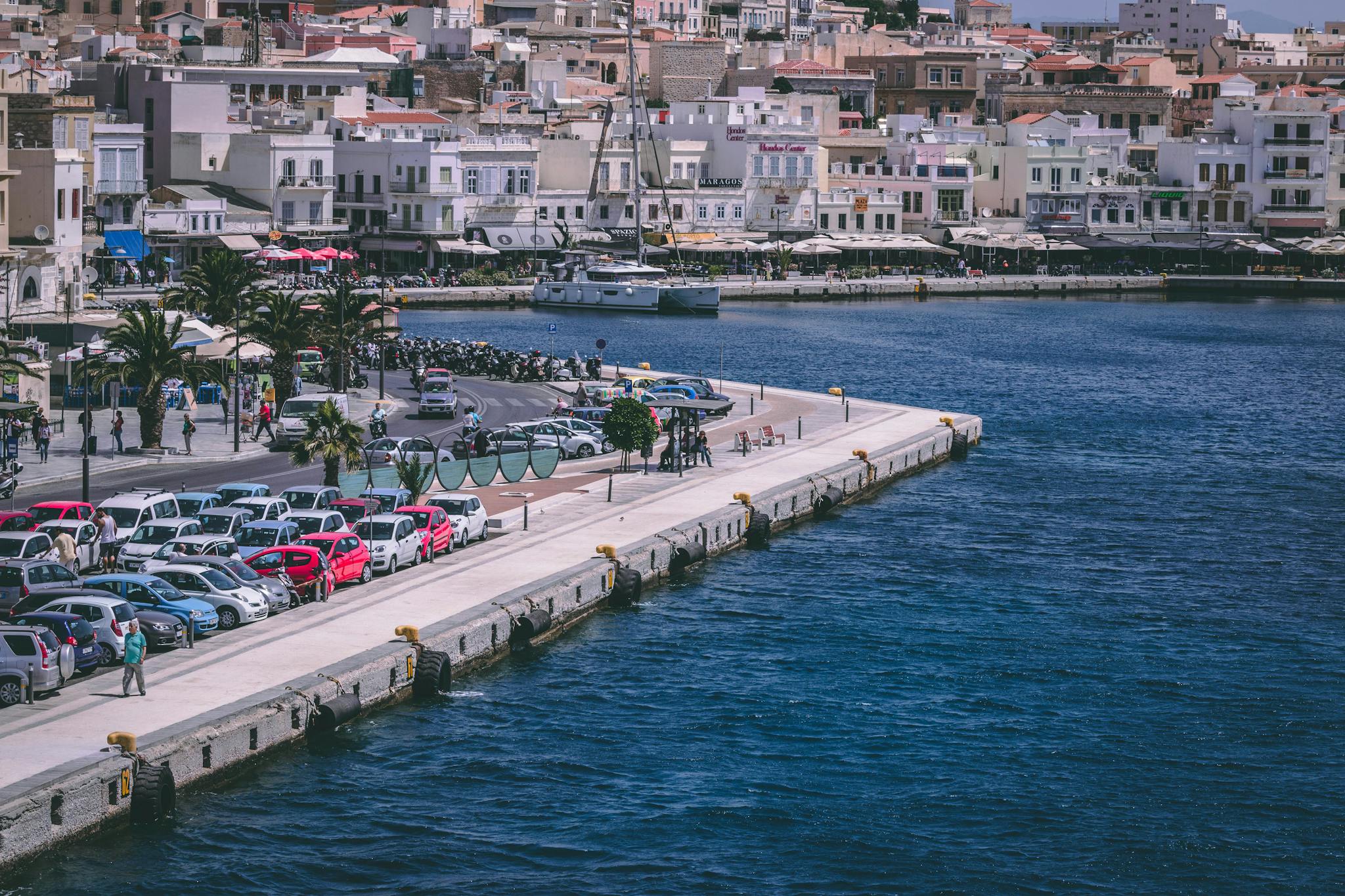 Scenic view of a bustling harbor with parked cars, vibrant buildings, and clear blue water.