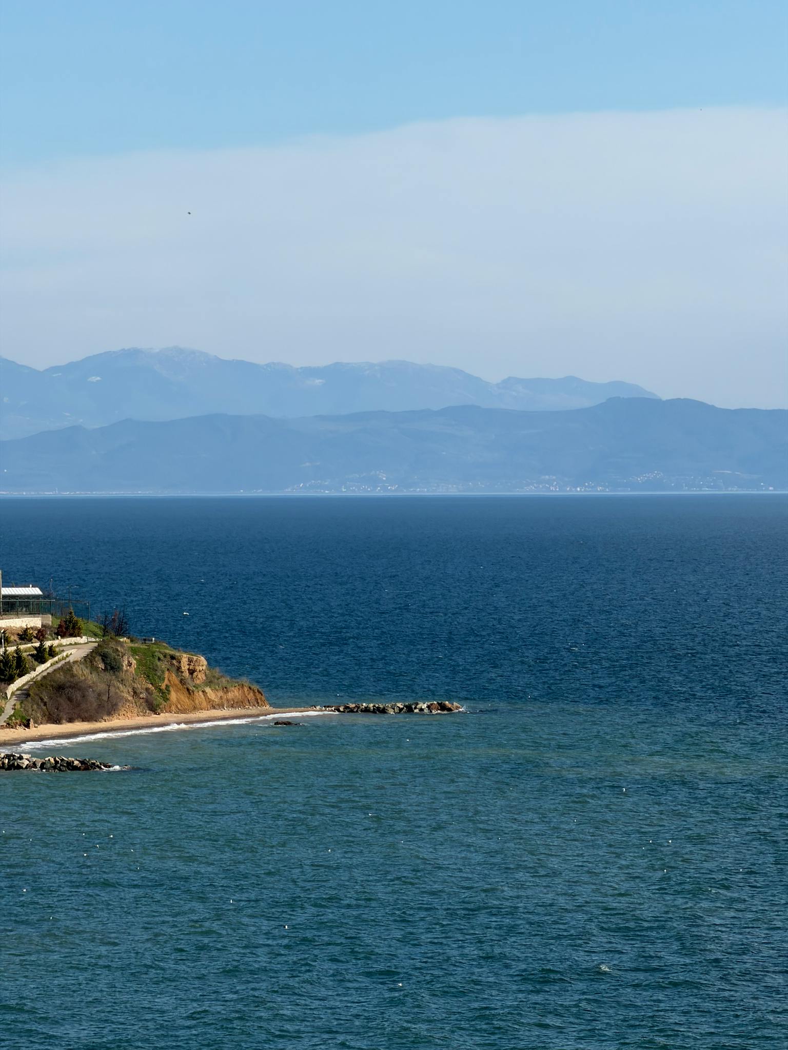 Serene coastal landscape with blue sea and distant mountains under clear sky.